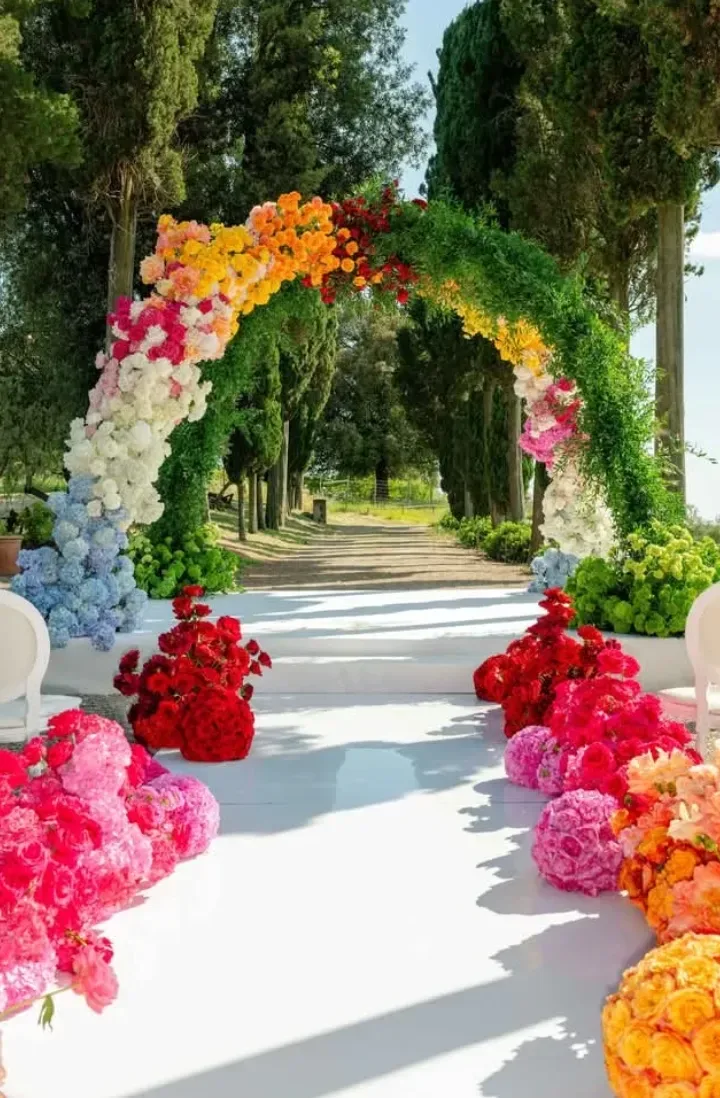 Arco floreale con rose bianche, rosa, gialle e ortensie azzurre montato tra i cipressi di una villa in provincia di Terni