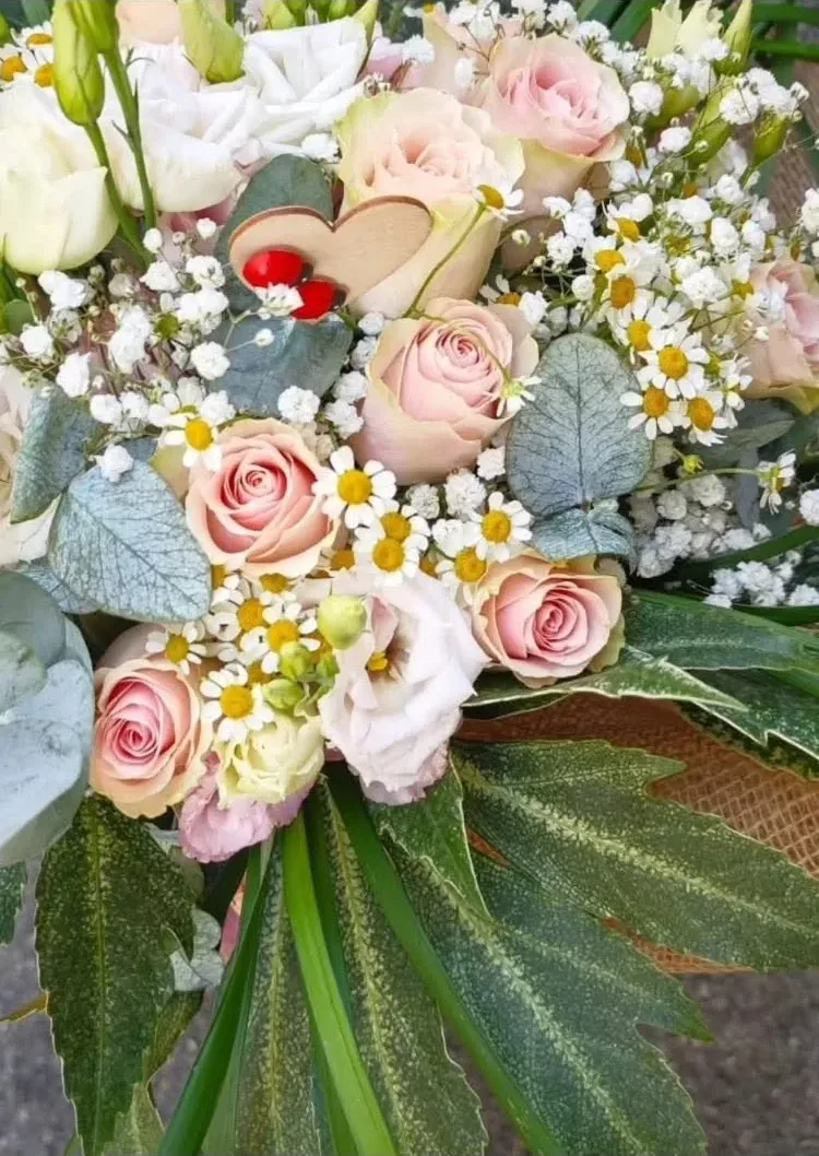 Mazzo pastello di rose cipria, lisianthus bianchi, camomilla e gypsophila con un cuoricino di legno tra i fiori