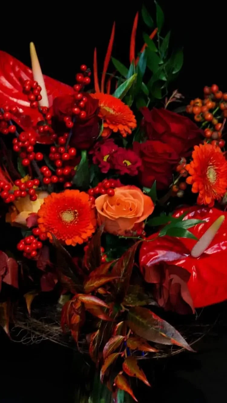 Composizione di rose rosse, gerbere arancioni, anthurium e bacche rosse su fondo scuro