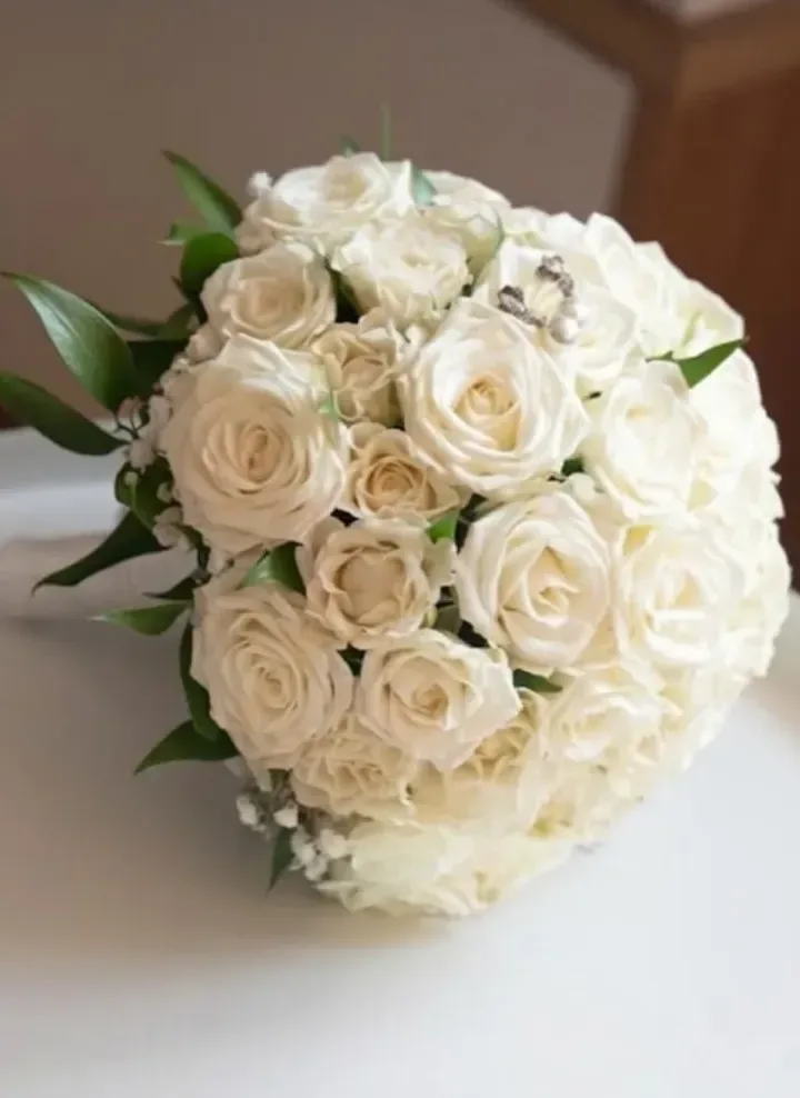 Bouquet da sposa rotondo di rose bianche e avorio con gypsophila, foglie di ruscus e spilla di strass sul gambo