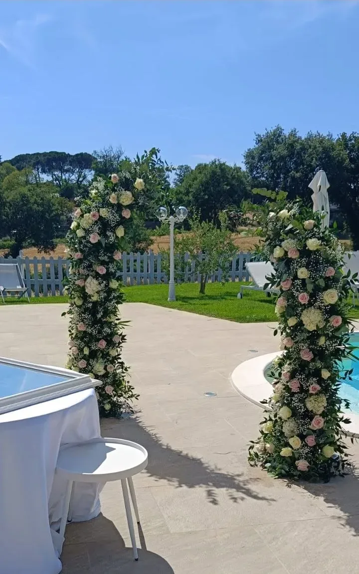 Due colonne fiorite di rose bianche e rosa e gypsophila ai lati del bordo piscina, in una villa per ricevimenti