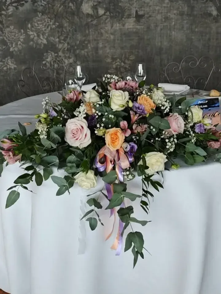 Composizione per il tavolo degli sposi con rose rosa e pesca, lisianthus, alstroemerie ed eucalipto cadente su tovaglia bianca